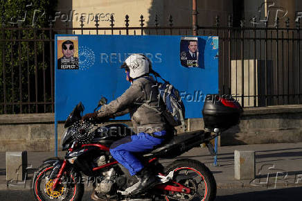 A motorcycle passes by electoral posters of Nicusor Dan and George Simion in Bucharest
