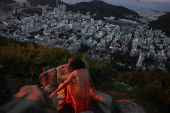A woman climbs rocks to take a photo during sunrise at Dona Marta lookout point in Rio de Janeiro