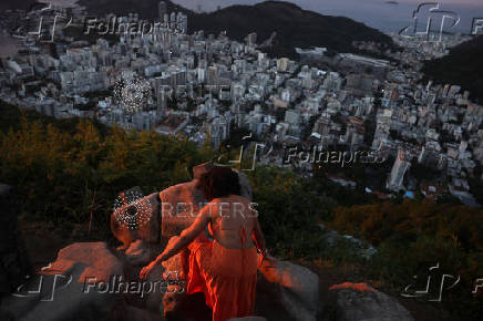 A woman climbs rocks to take a photo during sunrise at Dona Marta lookout point in Rio de Janeiro