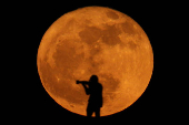 A photographer is silhouetted against the full moon known as the strawberry moon in Arinaga