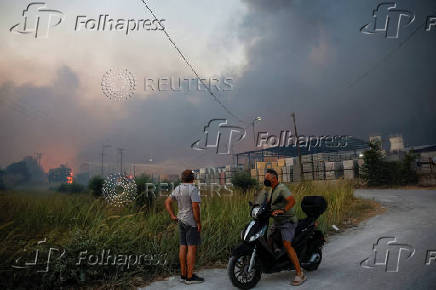People watch a fire at a cement factory sparked by a nearby wildfire, in Patras