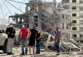 People stand together at a damaged site in the aftermath of Israeli strikes, at Beirut's southern suburbs