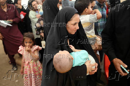 An Afghan woman deported from Iran, holds her child as she waits to register herself at a camp for returning migrants near the Islam Qala border crossing