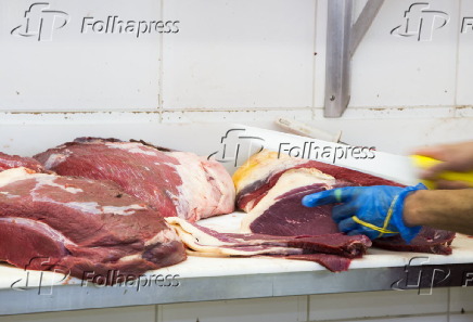 Açougueiro manipula peças de carnes em estabelecimento comercial especializado