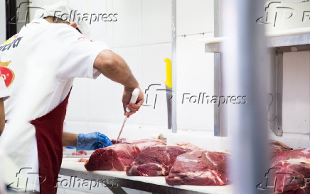 Açougueiro manipula peças de carnes em estabelecimento comercial especializado