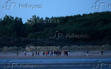 A group of migrants try to cross the beach to reach a dinghy whilst trying to cross the English Channel on a beach at Gravelines