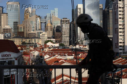 A worker climbs over a railing in the backdrop of the central business district skyline in Singapore