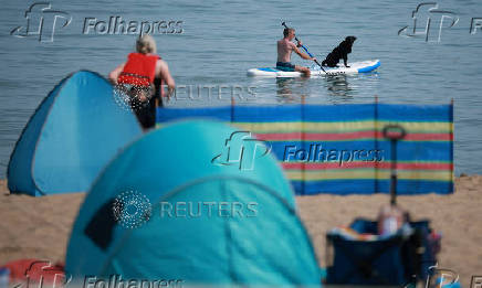 A man sits on a paddleboard with his dog near the beach at Rhos-on-Sea, Wales