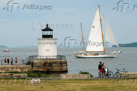A sailing yacht passes a lighthouse in Portland, Maine