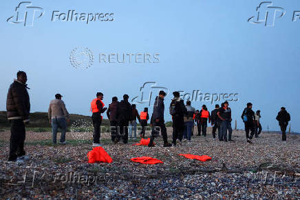 Migrants walk away from a beach after their inflatable dinghy was stopped, in Ambleteuse