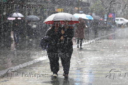 People use an umbrella to shelter from the rain as they walk along Pitt Street mall
