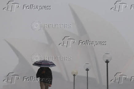 A person carrying an umbrella shelters from the rain as they walk past the Sydney Opera House