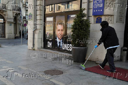 A woman cleans the street next to a poster of Nicusor Dan, in Bucharest