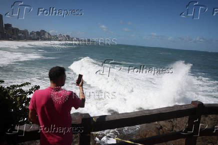 A man stands at a viewpoint on Leblon beach amid big waves in Rio de Janeiro
