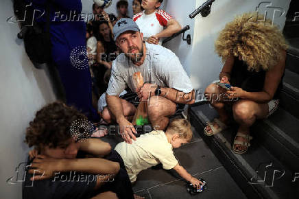 People take shelter opposite to the Meditarenean beach as siren sounds following missile attack from Iran on Israel, in Tel Aviv