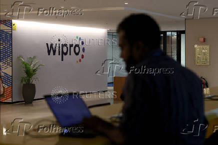 An employee works on his laptop near Wipro's logo inside the premises of the company in Bengaluru