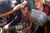 Palestinians wait to receive food cooked by a charity kitchen, in Khan Younis