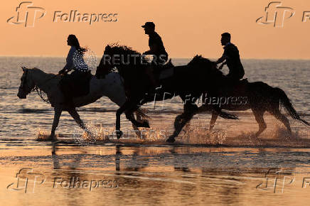 People ride horses during sunset as temperatures rise near Durres