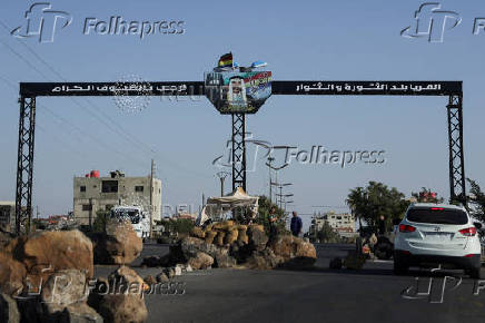 People gather near a sign signaling the entrance to the village of Al-Qurayya