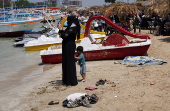 A woman holds her phone as she stands near the beach in Latakia