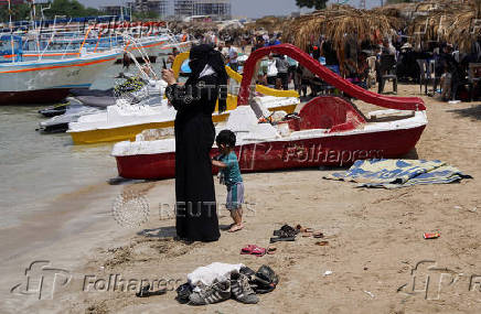 A woman holds her phone as she stands near the beach in Latakia