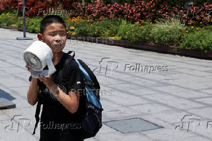 A child holds a portable fan amid a yellow alert for heat, in Shanghai
