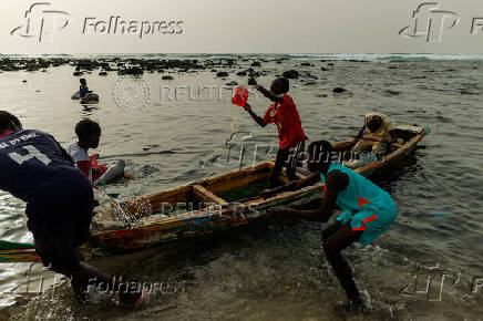 Children play as fishermen on a boat at the fishing port in Yoff beach