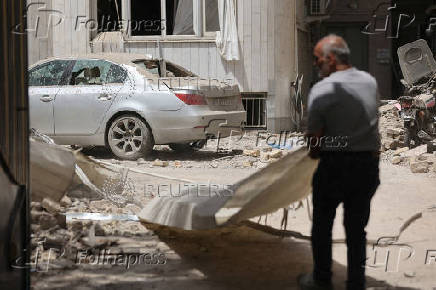 FILE PHOTO: A man stands near a damaged car at an impacted residential site, following an Israeli strike on Monday, after the ceasefire between Israel and Iran, in Tehran