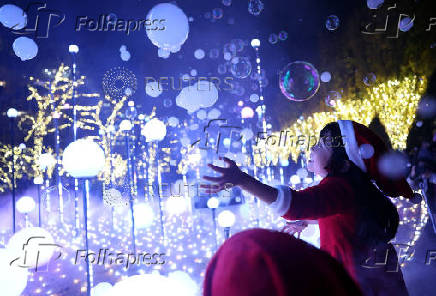A girl wearing a Santa Claus costume tries to catch soap bubbles in the air at an illumination event celebrating the upcoming the Christmas season at a park in Tokyo