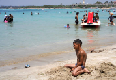 A boy sits near the water as people swim at a public beach in Latakia