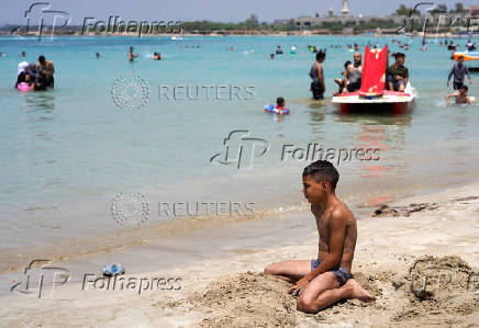 A boy sits near the water as people swim at a public beach in Latakia