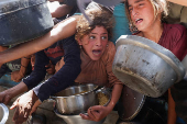 Palestinians wait to receive food cooked by a charity kitchen, in Khan Younis