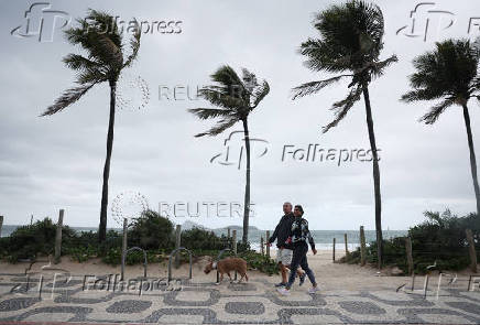 People walk along the Ipanema beach amid strong winds in Rio de Janeiro