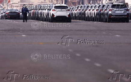 A worker is seen among newly manufactured cars awaiting export at a port in Yokohama