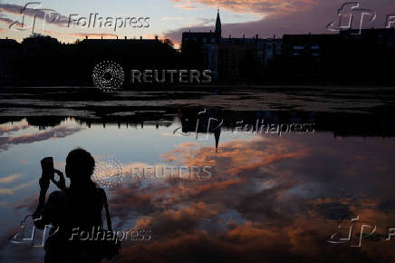 A person takes a picture at Sortedam Lake as the sun sets in Copenhagen